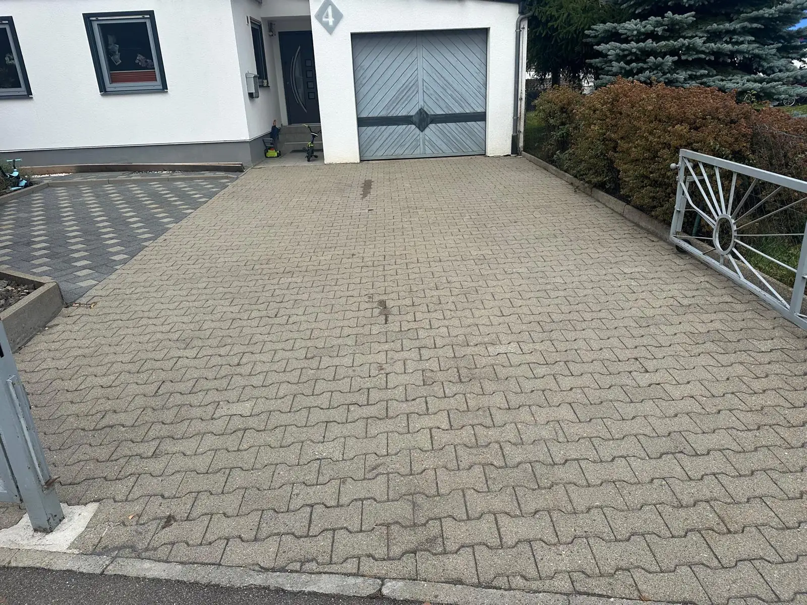 Gepflasterte Einfahrt vor einer Garage, links bemoost und braun verfärbt, rechts nach der Reinigung., nach der Reinigung