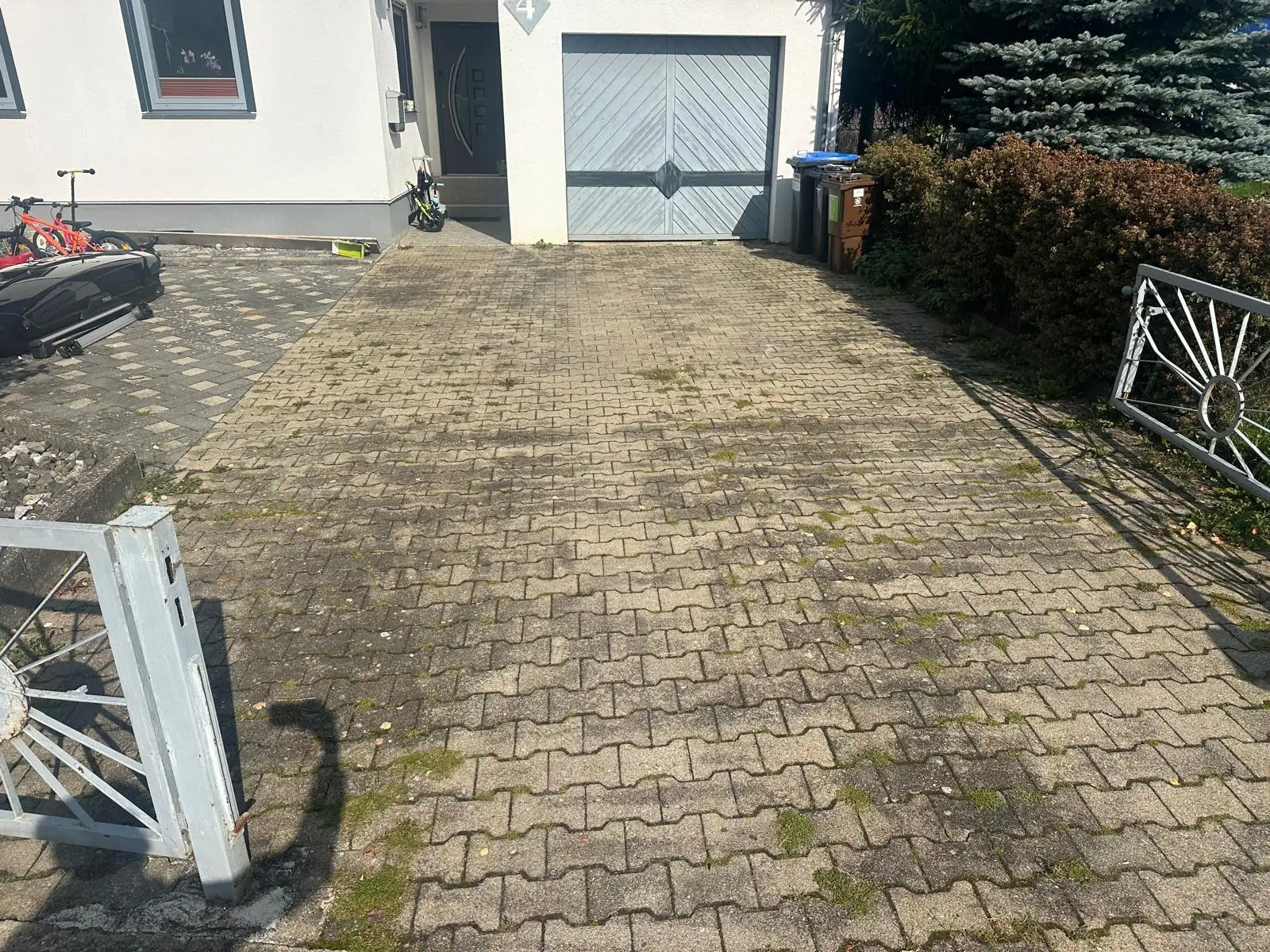 Gepflasterte Einfahrt vor einer Garage, links bemoost und braun verfärbt, rechts nach der Reinigung., vor der Reinigung