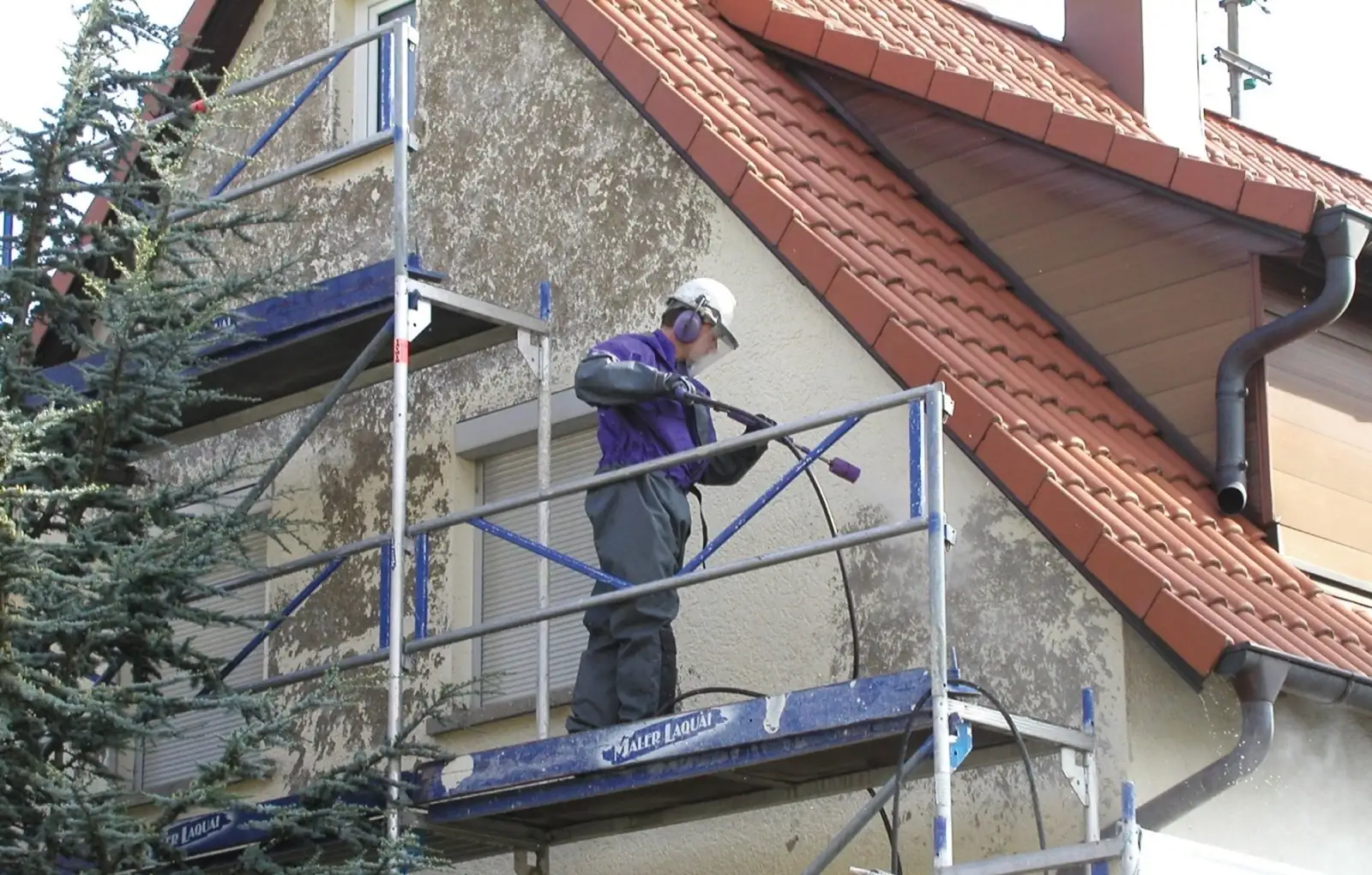 Eine Hausfassade wird vom Gerüst aus mit Heißwasser gereinigt