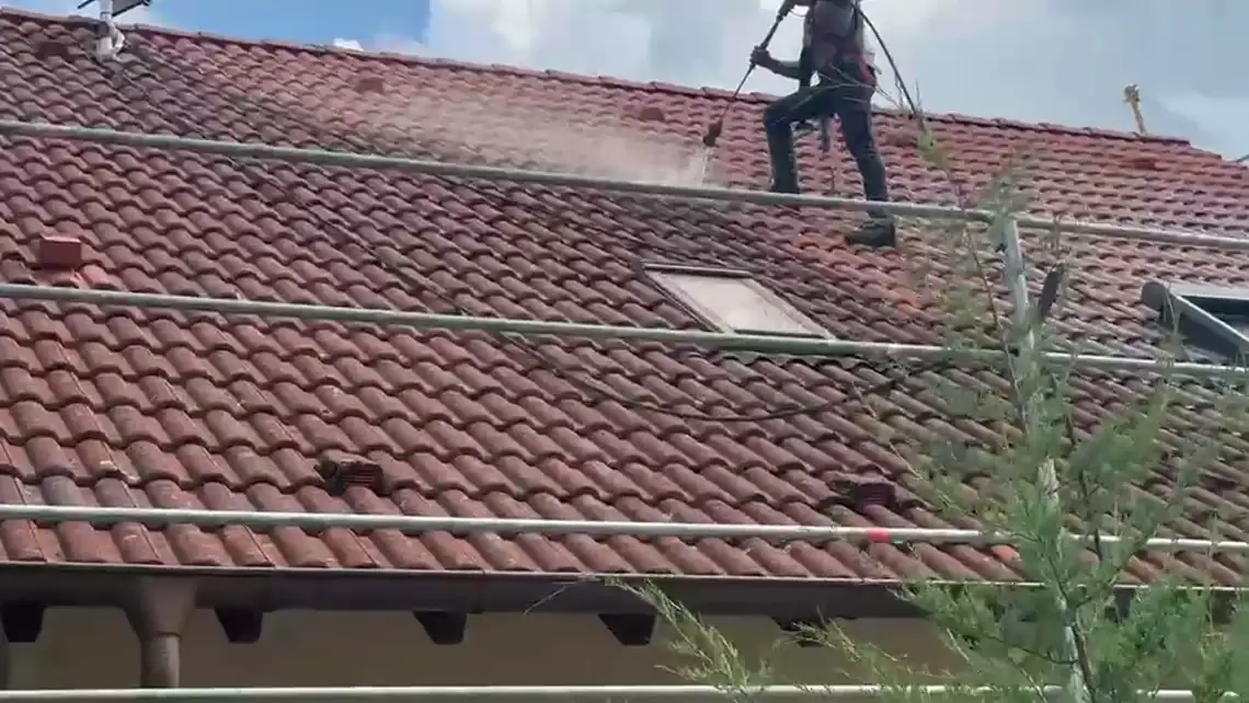 Ein Mitarbeiter arbeitet sich auf einem Ziegeldach mit der Lanze abwärts, vor ihm steht eine Wolke aus Wasserdampf.