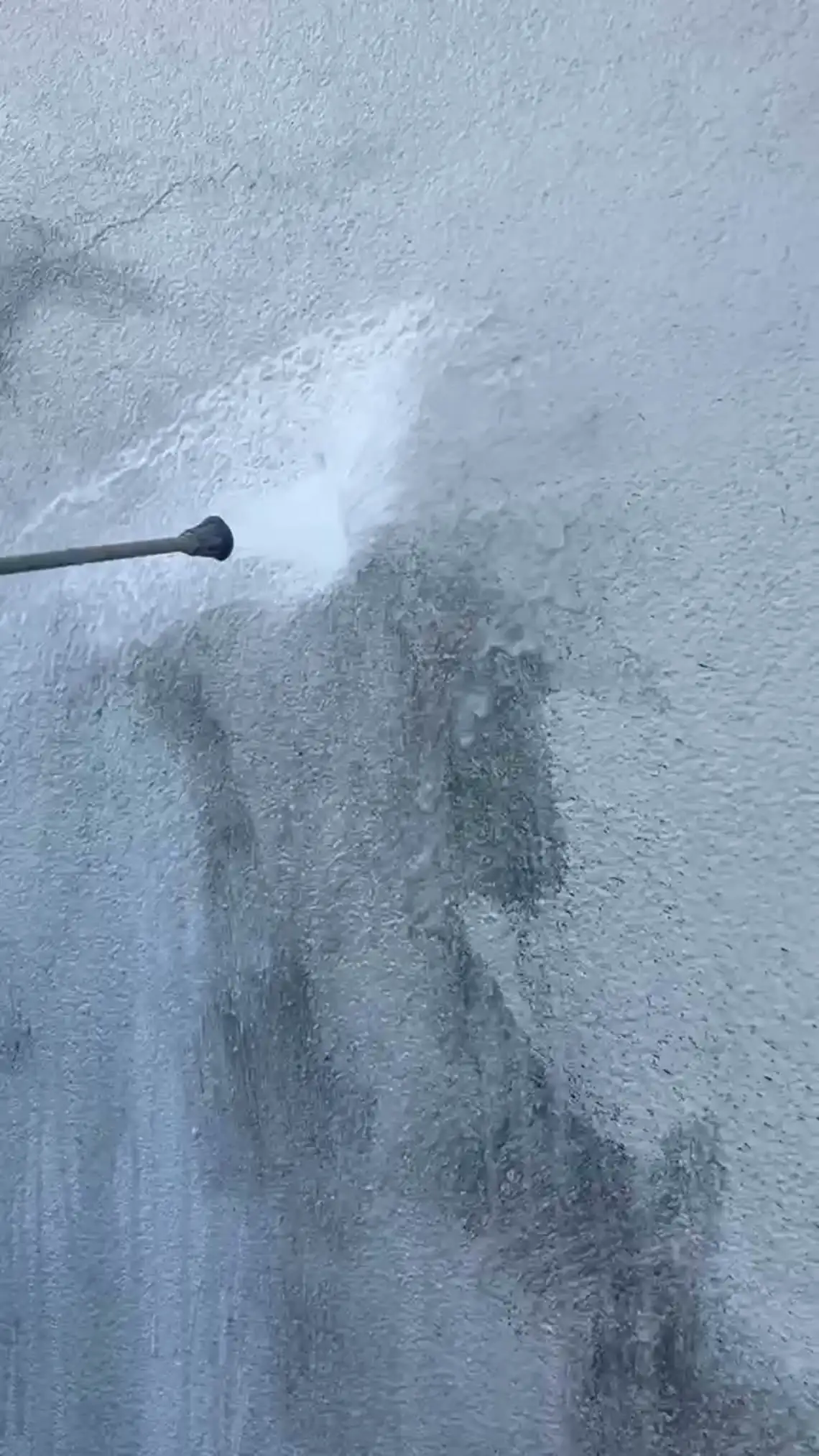 Ein Wasserstrahl trifft auf eine besprühte Betonwand, die Farbe löst sich unter dem Strahl und läuft in Schlieren nach unten.