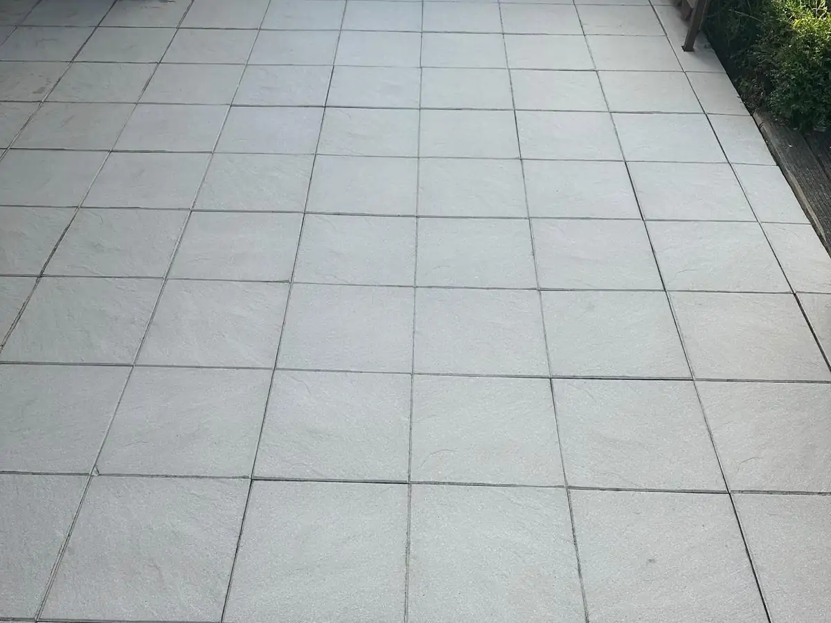 Plattenbelag an einem Wohnhaus, links grau mit Bewuchs in den Fugen, rechts nach der Reinigung., nach der Reinigung