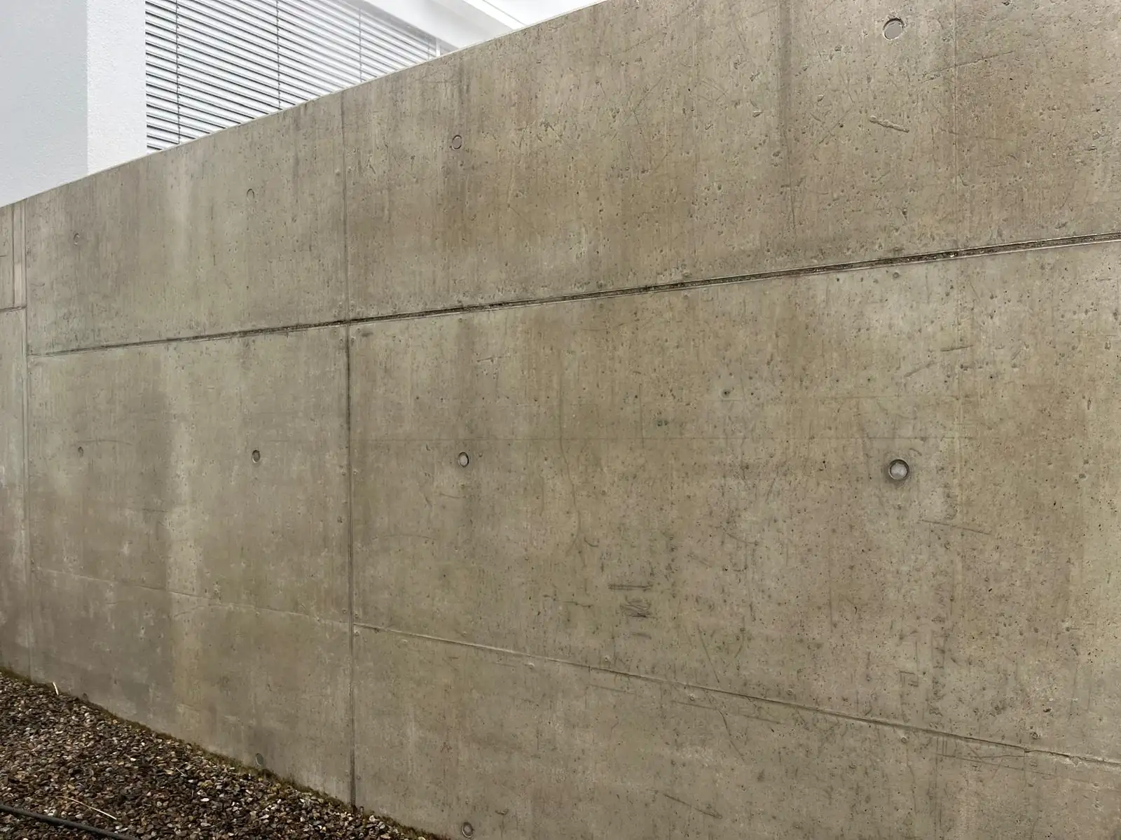 Sichtbetonmauer an einem Wohnhaus, links im ungereinigten Zustand mit braunen Ablaufspuren, rechts nach der Reinigung gleichmäßig grau., nach der Reinigung