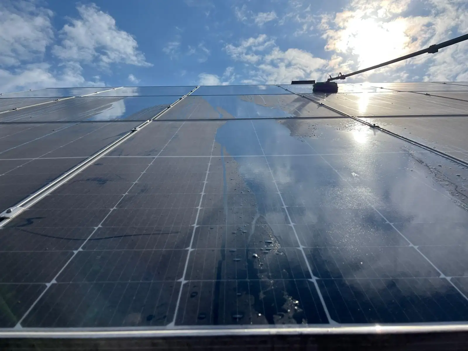 Solarmodule auf einem Schrägdach während der Reinigung, die linke Modulreihe ist bereits klar, auf der rechten liegt noch ein grauer Film.